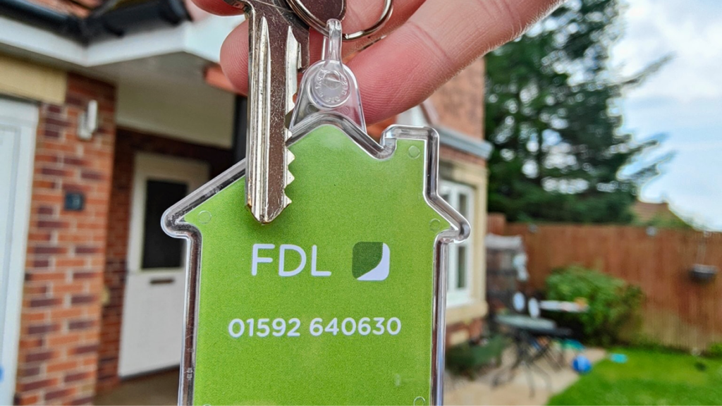 Someone holding an FDL-branded key fob outside a home